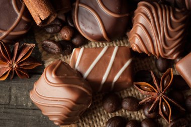 Koyu, beyaz ve sütlü çikolata yığını, cips çeşitleri. Kaba ahşap arka planda çikolata ve kahve çekirdekleri. Baharatlar, tarçın. Seçici makro odaklanma. Çikolata arkaplanı. Tatlılar