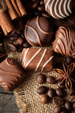 Koyu, beyaz ve sütlü çikolata yığını, cips çeşitleri. Kaba ahşap arka planda çikolata ve kahve çekirdekleri. Baharatlar, tarçın. Seçici makro odaklanma. Çikolata arkaplanı. Tatlılar