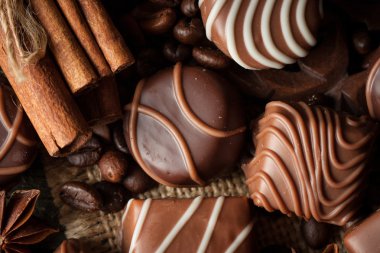 Koyu, beyaz ve sütlü çikolata yığını, cips çeşitleri. Kaba ahşap arka planda çikolata ve kahve çekirdekleri. Baharatlar, tarçın. Seçici makro odaklanma. Çikolata arkaplanı. Tatlılar