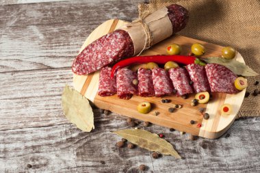 Italian salami with olives and spices on wooden background clipart
