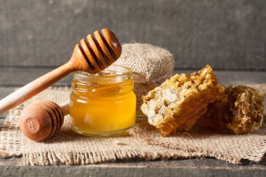 Tatlım gelen ahşap bal ayı gri rustik ahşap arka plan üzerinde bir kavanoza damlama