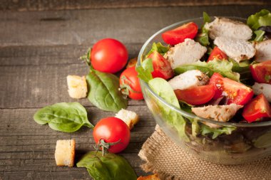 Taze salata domates, ruccola, tavuk göğsü, roka, kraker ve baharat yapılmış. Ahşap arka plan üzerinde beyaz, şeffaf bir kasede Sezar salatası