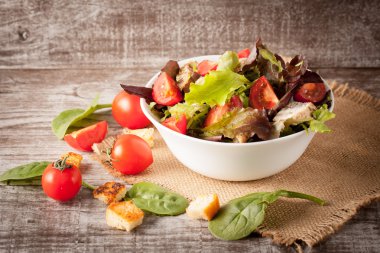 Taze salata domates, ruccola, tavuk göğsü, roka, kraker ve baharat yapılmış. Ahşap arka plan üzerinde beyaz, şeffaf bir kasede Sezar salatası