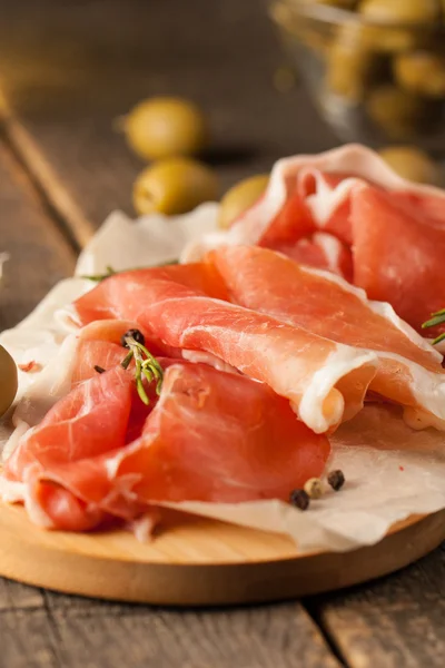 Primer plano de rodajas finas de jamón con aceitunas mixtas y pimentón sobre tabla de cortar de madera — Foto de Stock