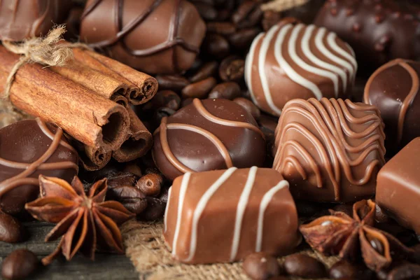 Koyu, beyaz ve sütlü çikolata yığını, cips çeşitleri. Kaba ahşap arka planda çikolata ve kahve çekirdekleri. Baharatlar, tarçın. Seçici makro odaklanma. Çikolata arkaplanı. Tatlılar