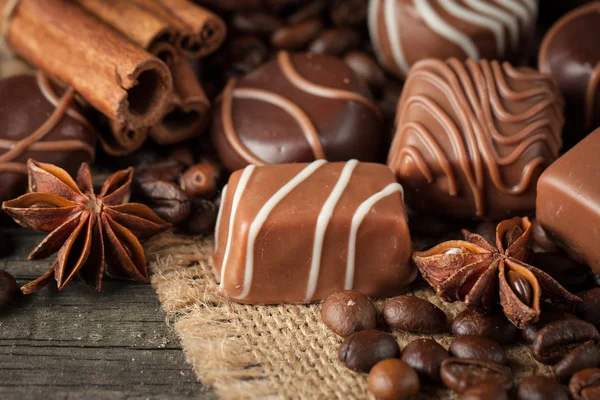 Koyu, beyaz ve sütlü çikolata yığını, cips çeşitleri. Kaba ahşap arka planda çikolata ve kahve çekirdekleri. Baharatlar, tarçın. Seçici makro odaklanma. Çikolata arkaplanı. Tatlılar