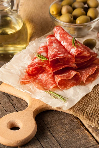 Italian salami with olives and spices on wooden background — Stock Photo, Image