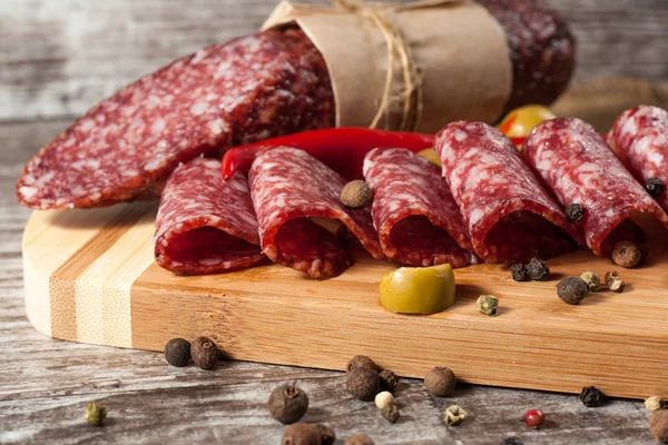 Salami italiano con aceitunas y especias sobre fondo de madera — Foto de Stock