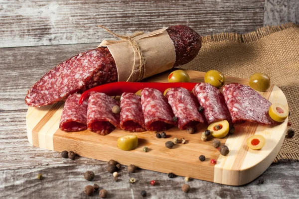 Salami italiano con aceitunas y especias sobre fondo de madera — Foto de Stock