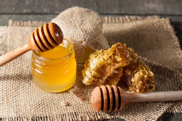 Honig tropft aus einem hölzernen Honiglöffel in einem Glas auf hölzernem grauem rustikalem Hintergrund — Stockfoto