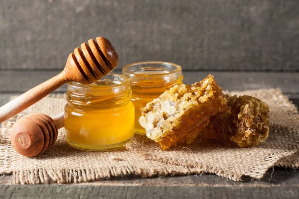 Miel goteando de un tarro de miel de madera sobre fondo rústico gris madera —  Fotos de Stock