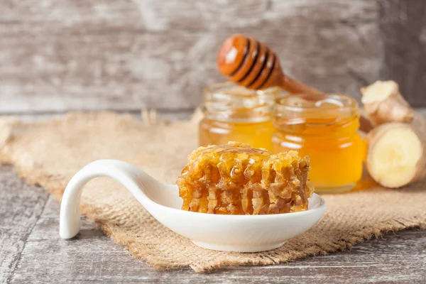 Honey dripping from a wooden honey dipper in a jar on wooden grey rustic background — Stock Photo, Image