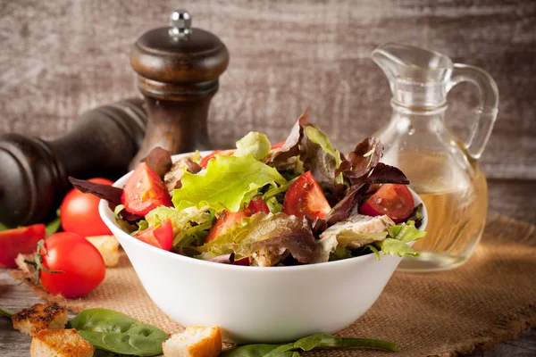 Ensalada fresca de tomate, ruccola, pechuga de pollo, rúcula, galletas saladas y especias. Ensalada César en un bol blanco y transparente sobre fondo de madera —  Fotos de Stock