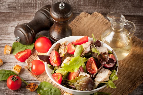 Salată proaspătă din roșii, ruccola, piept de pui, arugula, biscuiți și condimente. Salată de cezar într-un castron alb, transparent pe fundal din lemn — Fotografie, imagine de stoc