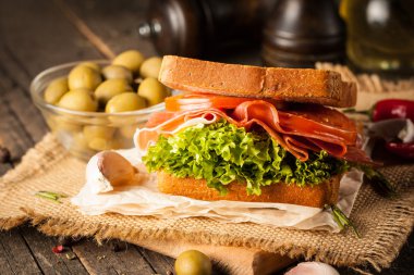 Club sandviç yakın çekim fotoğraf. Sandviçle tanışın, jambon, salam, salata, sebze, marul, domates, soğan ve hardal ahşap arka plan üzerinde taze dilimlenmiş siyah ekmek üzerinde. Zeytin arka plan.