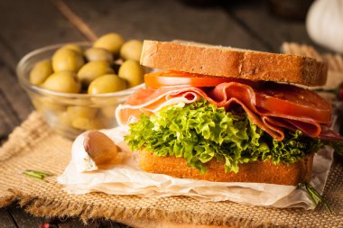 Club sandviç yakın çekim fotoğraf. Sandviçle tanışın, jambon, salam, salata, sebze, marul, domates, soğan ve hardal ahşap arka plan üzerinde taze dilimlenmiş siyah ekmek üzerinde. Zeytin arka plan.