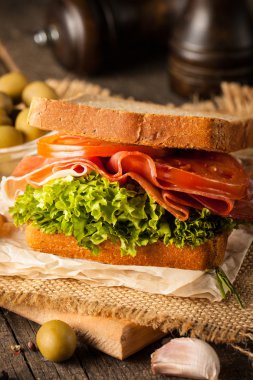 Club sandviç yakın çekim fotoğraf. Sandviçle tanışın, jambon, salam, salata, sebze, marul, domates, soğan ve hardal ahşap arka plan üzerinde taze dilimlenmiş siyah ekmek üzerinde. Zeytin arka plan.