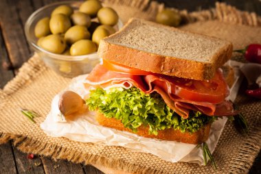 Club sandviç yakın çekim fotoğraf. Sandviçle tanışın, jambon, salam, salata, sebze, marul, domates, soğan ve hardal ahşap arka plan üzerinde taze dilimlenmiş siyah ekmek üzerinde. Zeytin arka plan.