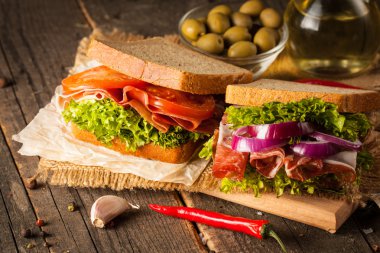 Club sandviç yakın çekim fotoğraf. Sandviçle tanışın, jambon, salam, salata, sebze, marul, domates, soğan ve hardal ahşap arka plan üzerinde taze dilimlenmiş siyah ekmek üzerinde. Zeytin arka plan.