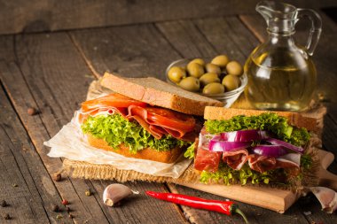 Club sandviç yakın çekim fotoğraf. Sandviçle tanışın, jambon, salam, salata, sebze, marul, domates, soğan ve hardal ahşap arka plan üzerinde taze dilimlenmiş siyah ekmek üzerinde. Zeytin arka plan.