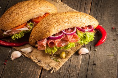 Club sandviç yakın çekim fotoğraf. Sandviçle tanışın, jambon, salam, salata, sebze, marul, domates, soğan ve hardal ahşap arka plan üzerinde taze dilimlenmiş siyah ekmek üzerinde. Zeytin arka plan.