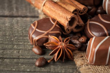 Koyu, beyaz ve sütlü çikolata yığını, cips çeşitleri. Kaba ahşap arka planda çikolata ve kahve çekirdekleri. Baharatlar, tarçın. Seçici makro odaklanma. Çikolata arkaplanı. Tatlılar