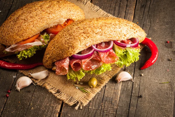 Close-up photo of a club sandwich. Sandwich with meet, prosciutto, salami, salad, vegetables, lettuce, tomato, onion and mustard on a fresh sliced rye bread on wooden background. Olives background.