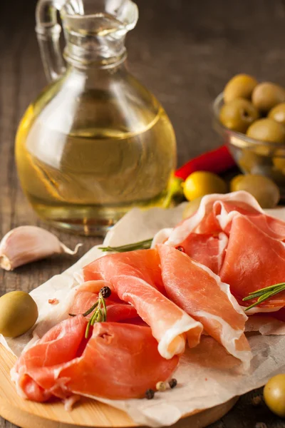 Close-up de fatias finas de prosciutto com azeitonas misturadas e páprica na placa de corte de madeira — Fotografia de Stock