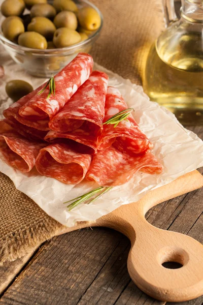 Italian salami with olives and spices on wooden background — Stock Photo, Image