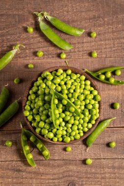 Tahta masadaki bir kasede taze bezelye ve kabuklar. Sebzeli sağlıklı yiyecek..