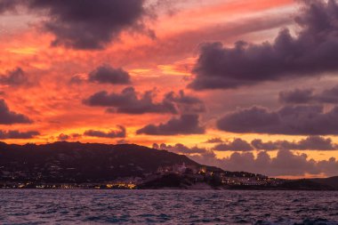 Korsika 'nın Balagne bölgesindeki antik kalenin ve Calvi kasabasının ışıkları üzerinde turuncu gün batımı ön planda Akdeniz ile birlikte