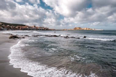 Waves washing onto the sandy beach of Ile Rousse in the Balagne region of Corsica after storm Hortense with the red rock of La Pietra, the harbour and town in the distance