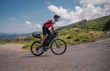 Speloncato, Corsica, France - 9th June 2021: Thomas Dupin competing in the 2021 BikingMan Corsica race after 780km at the village of Speloncato. Biking Man Corsica is an annual 1000km endurance cycling event circling the island unsupported. clipart