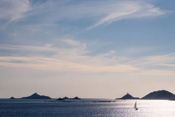 セーリングヨットとスーパーヨットは コルシカ島のAjaccio近くのLes Iles Sanguinairesの穏やかな塔と灯台を通り 地中海を照らす太陽の光で青い午後の空にシルエットになっています — ストック写真