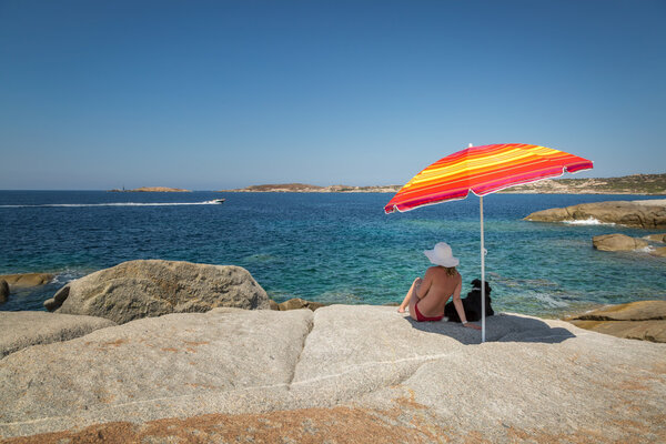 Женщина в красном бикини и белой шляпе под зонтиком смотрит на С
