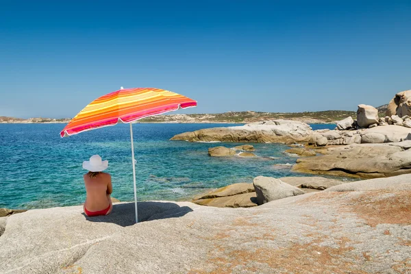 Woman in red bikini and white hat under parasol looking out to s