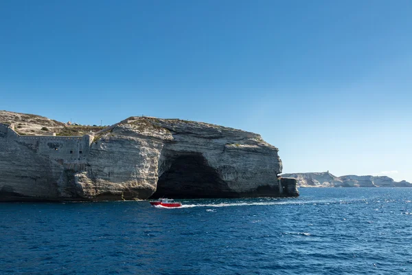 Bateau rouge passant grotte dans les falaises blanches à Bonifacio — Photo