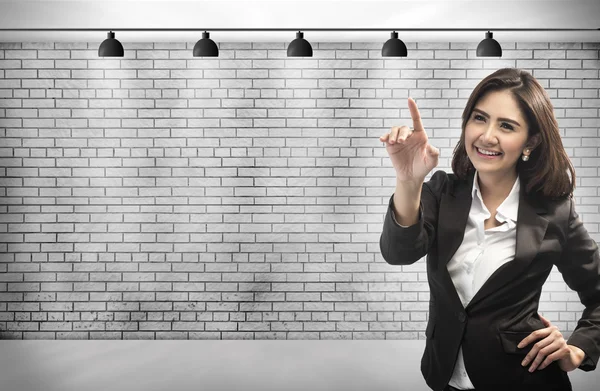 Γυναίκα των επιχειρήσεων αγγίζοντας μια φανταστική οθόνη με το δάχτυλό της. σε φόντο τοίχο τούβλου με αντίγραφο χώρου για το σχέδιό σας. — Φωτογραφία Αρχείου