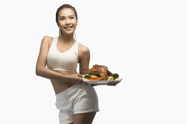 Young woman with perfect body holding and showing roast chicken — Stock Photo, Image