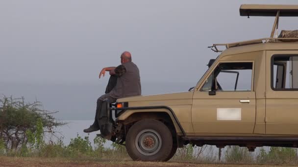 一名男性游客驾驶Safari Vehicle观赏非洲风景 坐着旅行度假旅行单人游览独木舟看起来像老人丰田越野车看到旅行无毛游览 — 图库视频影像