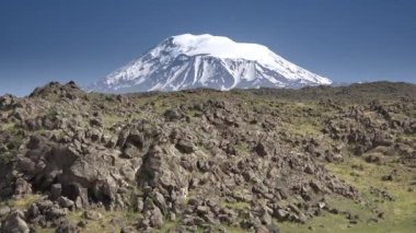 Volkanik karlı dağ zirvesinin önündeki donmuş lav bazalt kayaları. Yüksek irtifa dağ zirvesi. Kilimanjaro yanardağının tepesi. Büyük ölçekli erozyon 4K dağ UHD eksikliği nedeniyle volkanik yapının iç kısmının jeolojisi kötü biliniyor.