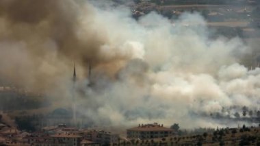 Şehir evlerinin kenarında çalılık orman yangını. Kasaba köyü yerleşim alanı. Alev alev yanan flama dumanı. Telezomu çevreleyen geniş bir alana yayılmış.