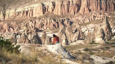 Göz kamaştırıcı kırmızı kumtaşı hoodoos manzarasında oturan bir kadın. Ulusal park büyücüsü genç kız çadır çadırı, kaya perisi baca piramit kanyon kapadokya doğa insanlar kurak drenaj havzası badland turistik tortu 4K