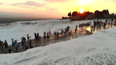 Ziyaretçiler ve turistler kalsiyum karbonat geçitlerini geziyorlar. Travertin teras oluşumları. Sıcak pınardan gelen sular tarafından birikmiş editörlük kayaları. Pamukkale pamuk kalesi doğal kireçtaşı kalesi anadolu sakinli seyahat jeolojisi 4K