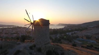 Günbatımında deniz kenarındaki eski tarihi yel değirmeni. Rüzgâr enerjisi açısal kinetik enerji yelkenleri antik taş yelkenleri yatay, içi boş kule mekaniği dikey tarımsal hava görüntüsü uçuş dronu üzerinde çalışır..