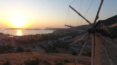 Günbatımında deniz kenarındaki eski tarihi yel değirmeni. Rüzgâr enerjisi açısal kinetik enerji yelkenleri antik taş yelkenleri yatay, içi boş kule mekaniği dikey tarımsal hava görüntüsü uçuş dronu üzerinde çalışır..