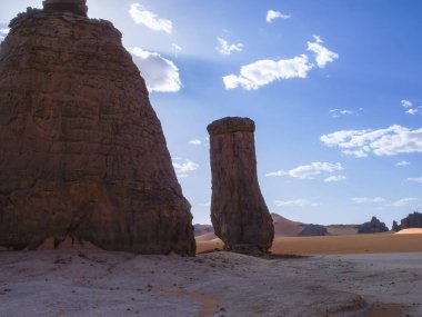 Sahra Çölü 'ndeki Kızıl Tadrart' ın kaya oluşumları ve altın tepecikleri. Berrak bir gökyüzünün altında çarpıcı bir doğal manzara. Sahra Çölü, Cezayir 'de gün doğumunda kum tepeleri ve kaya oluşumlarıyla Kızıl Tadrart' ın manzarası.