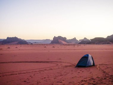 Sahra Çölü 'ndeki Kızıl Tadrart' ın kaya oluşumları ve altın tepecikleri. Berrak bir gökyüzünün altında çarpıcı bir doğal manzara. Sahra Çölü, Cezayir 'de gün doğumunda kum tepeleri ve kaya oluşumlarıyla Kızıl Tadrart' ın manzarası.