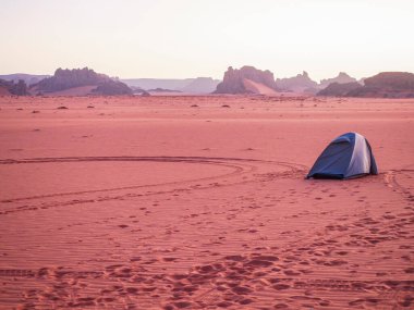 Sahra Çölü 'ndeki Kızıl Tadrart' ın kaya oluşumları ve altın tepecikleri. Berrak bir gökyüzünün altında çarpıcı bir doğal manzara. Sahra Çölü, Cezayir 'de gün doğumunda kum tepeleri ve kaya oluşumlarıyla Kızıl Tadrart' ın manzarası.