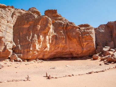 Sahra Çölü 'ndeki Kızıl Tadrart' ın kaya oluşumları ve altın tepecikleri. Berrak bir gökyüzünün altında çarpıcı bir doğal manzara. Sahra Çölü, Cezayir 'de gün doğumunda kum tepeleri ve kaya oluşumlarıyla Kızıl Tadrart' ın manzarası.